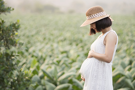 Una joven mujer embarazada tocando su vientre con felicidad mientras camina en la naturaleza.