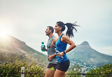 Un hombre y una mujer corriendo, cada uno lleva una botella de agua en su mano para rehidratarse después del ejercicio. 
