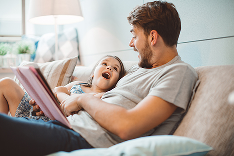 Un padre con su hija disfrutando de la lectura de un libro en su casa. 