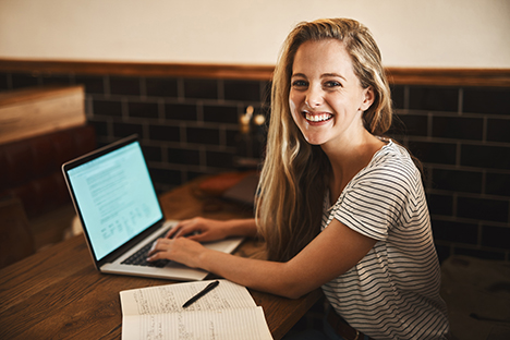 Una chica sonriente estudiando en un café,  aplicando el método Pomodoro para estudiar. 
