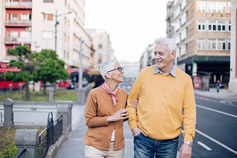 Una pareja de adultos mayores caminando y socializando en las calles de una ciudad. 
