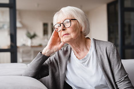 Una adulta mayor que padece ansiedad está viendo tristemente por la ventana.