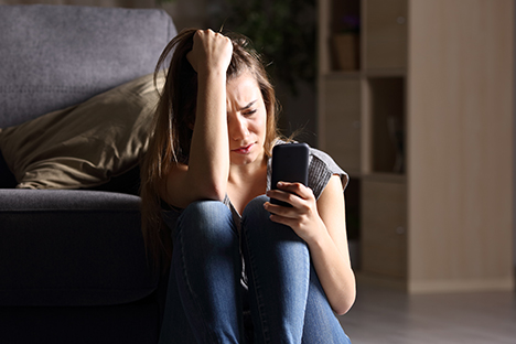 Una joven con depresión está viendo su teléfono móvil con tristeza. 