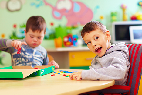 Dos niños con capacidades especiales jugando legos en un salón de clase. 