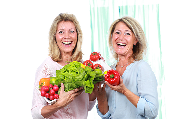 Dos mujeres adultas sosteniendo verduras en sus manos muy felizmente.